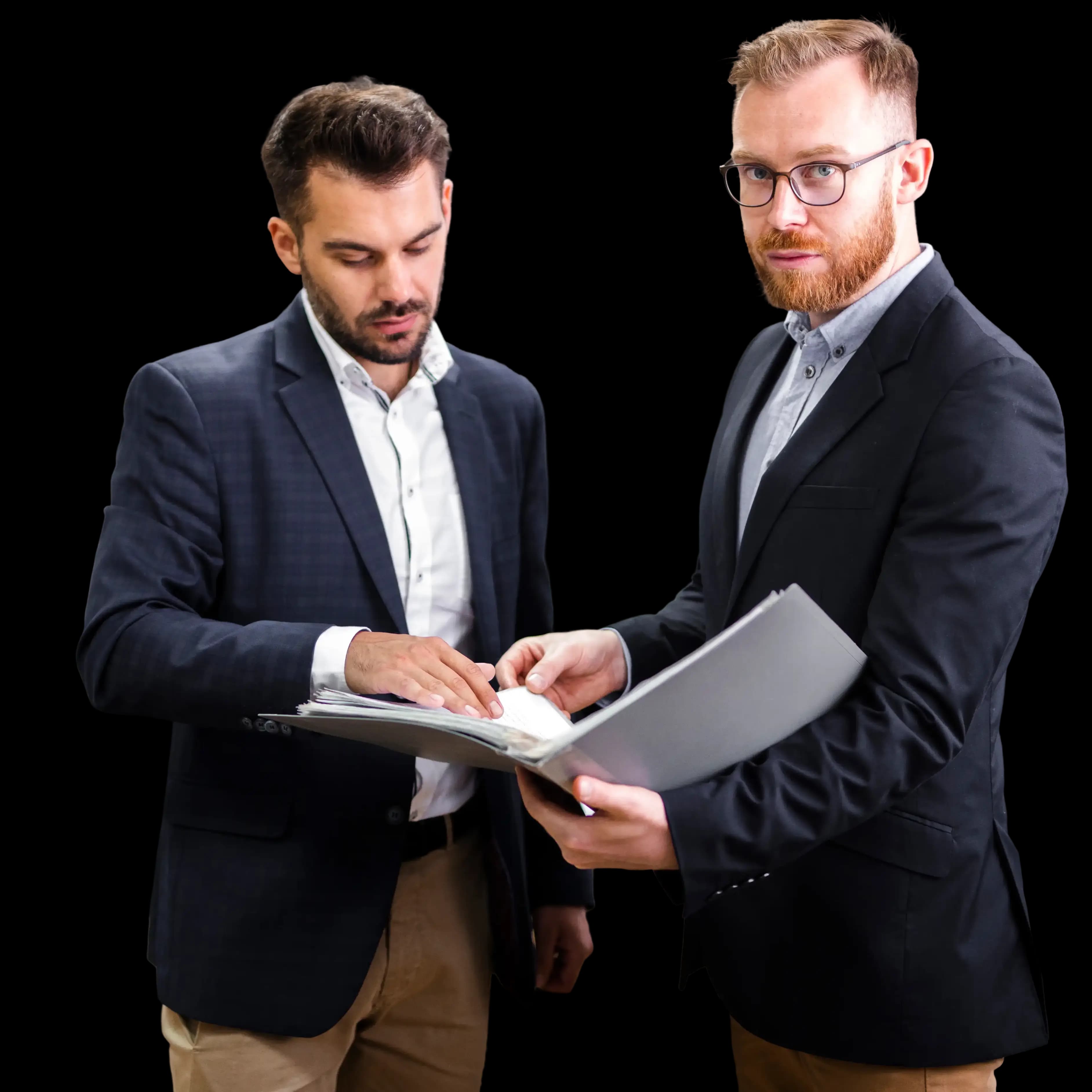 Two business professionals in formal attire reviewing paperwork together, one holding a folder and the other checking documents, demonstrating a careful and compliant business dissolution process.