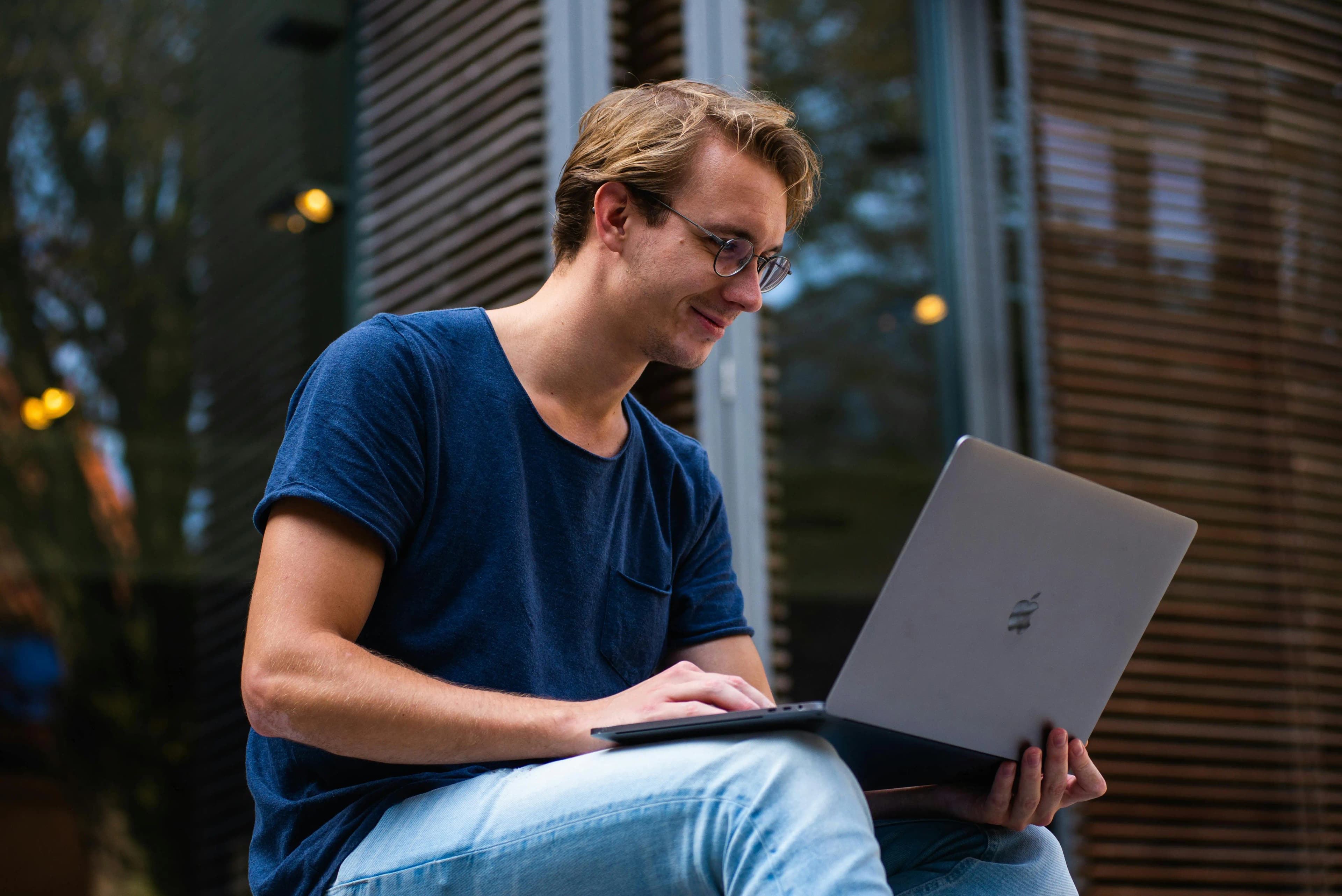 Individual business owner sitting in front of his house holding a laptop and smiling confidently, representing the ease and control of a sole proprietorship.