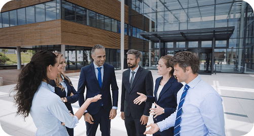 Group of six business professionals in formal attire having a discussion and smiling outside a modern office building