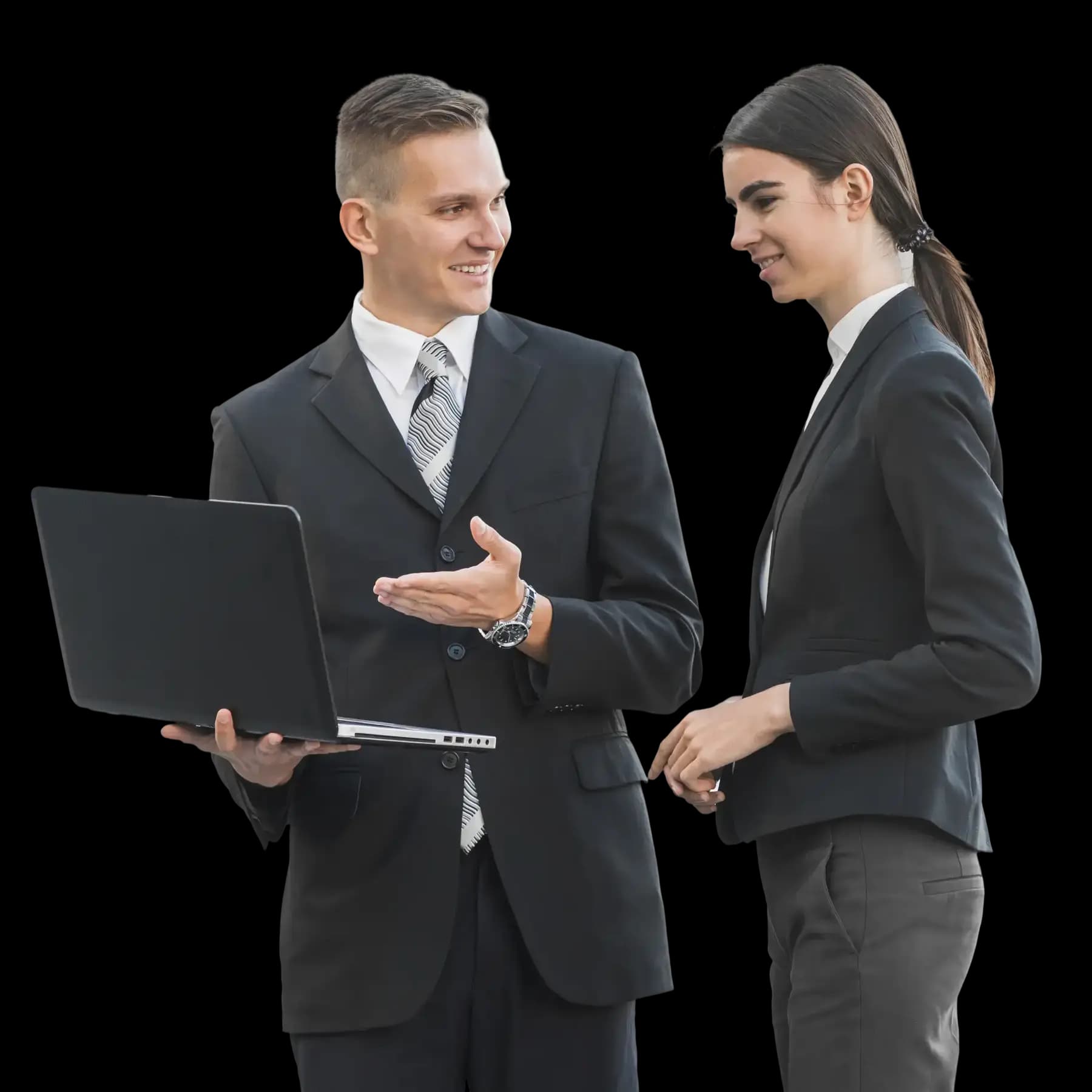 Two business professionals in formal attire standing together, one holding a laptop and pointing at the screen while the other reviews the information, representing teamwork and expert guidance during the business incorporation process.
