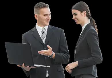 Two business professionals in formal attire standing together, one holding a laptop and pointing at the screen while the other reviews the information, representing teamwork and expert guidance during the business incorporation process.