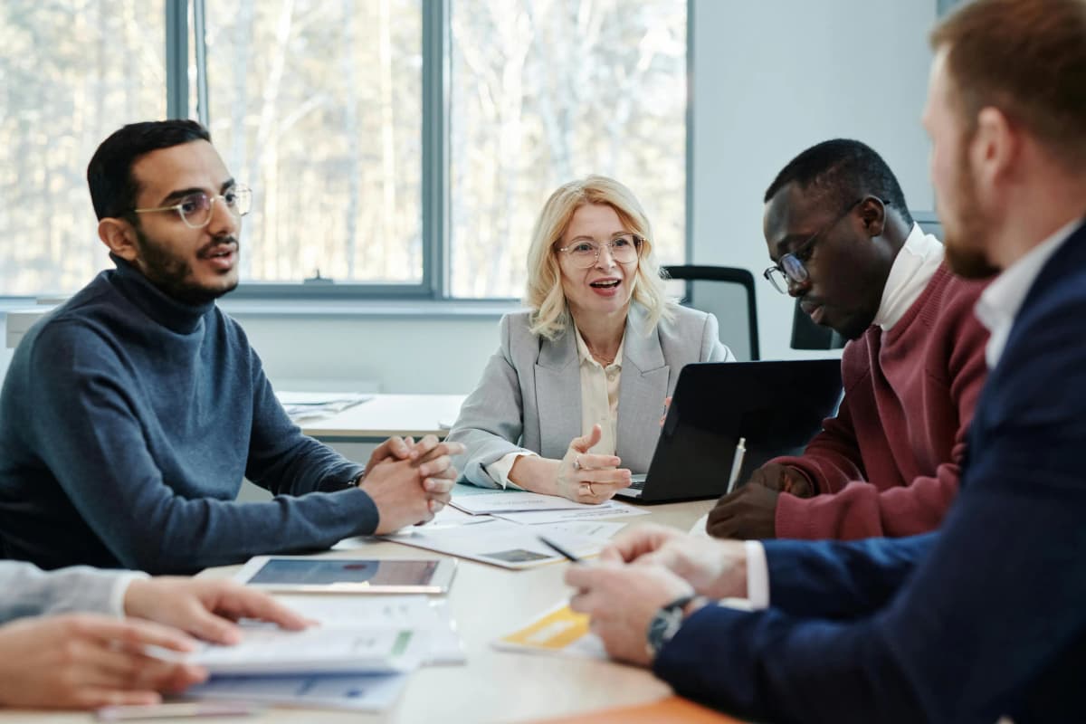 Four business professionals gathered around a desk with a laptop and paperwork, actively discussing strategies, demonstrating collaborative planning for successful business incorporation.