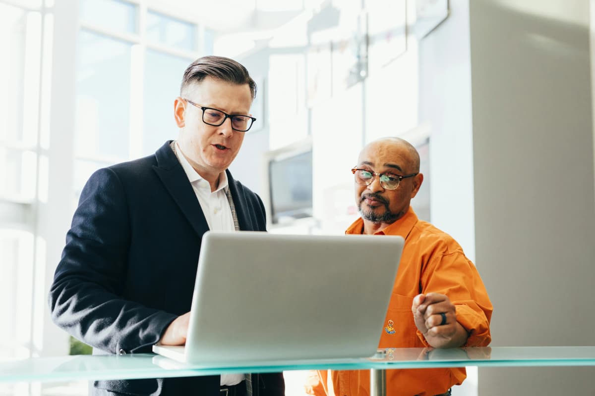 Two business professionals standing together in a modern office, collaborating while reviewing information on a laptop, representing strategic planning for professional corporation formation.