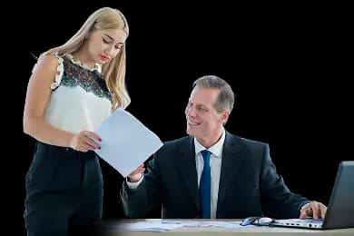 Two business professionals in formal attire, one standing and showing a document to the other who is seated at a desk with a laptop, paperwork, and sunglasses, illustrating collaborative review and decision-making for S Corporation election and IRS compliance.